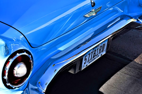 McCollisters Close-up of the rear end of a bright blue vintage car with chrome accents, a round tail light, and a license plate reading 57 TBIRD from Washington state.