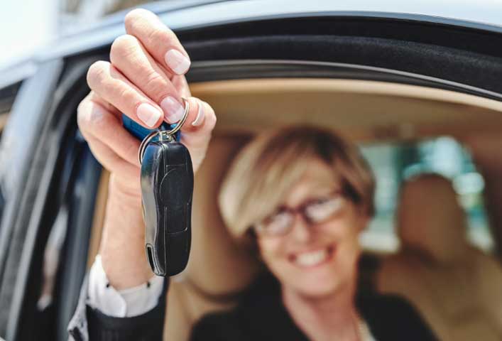 McCollisters A smiling person holds car keys out of a vehicle window, suggesting they are offering or showing the keys, highlighting convenient auto transport, with the car’s beige interior visible in the background.